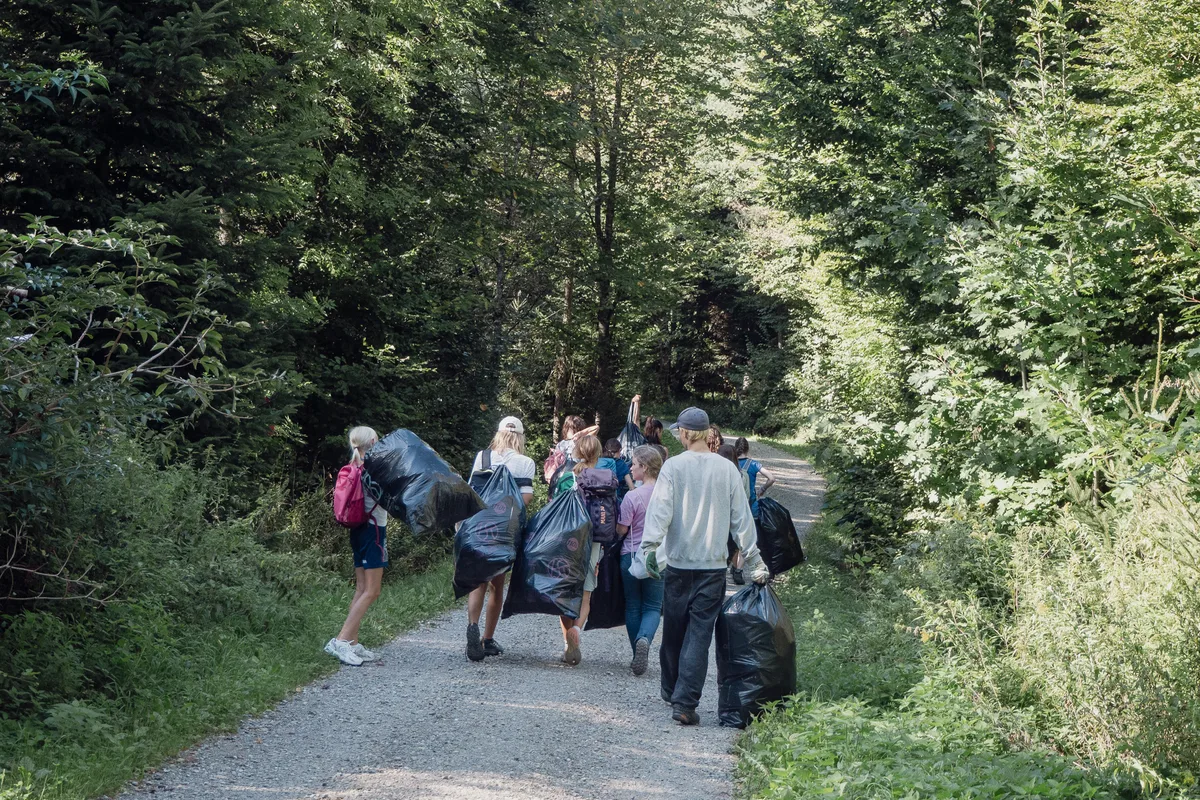 Eine Gruppe von Kindern und Jugendlichen läuft mit Abfallsäcken durch den Wald.